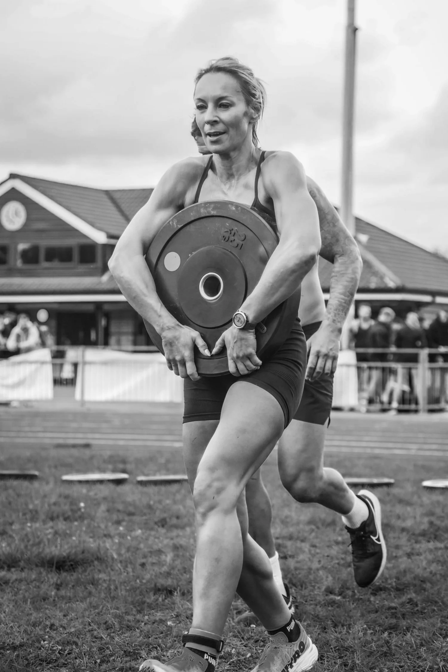 Atleet die een gewichtschijf aan de voorkant van het lichaam draagt in de ‘Front Carry Labour’-houding
