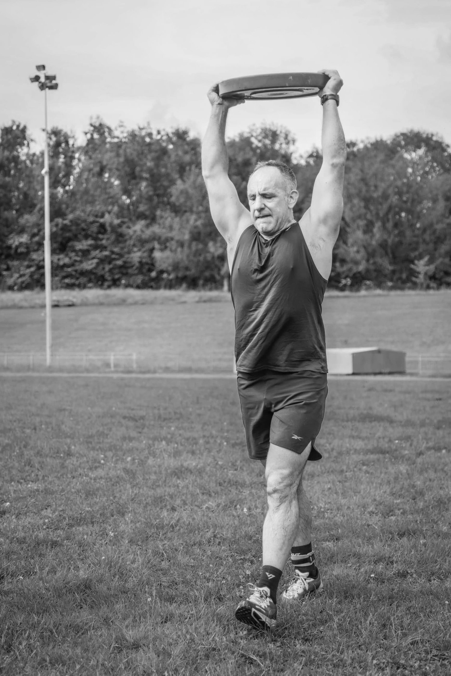 Atleet die een gewichtschijf boven het hoofd draagt tijdens de ‘Overhead Carry Labour’